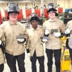Associates in welding gear holding completed practice welds.