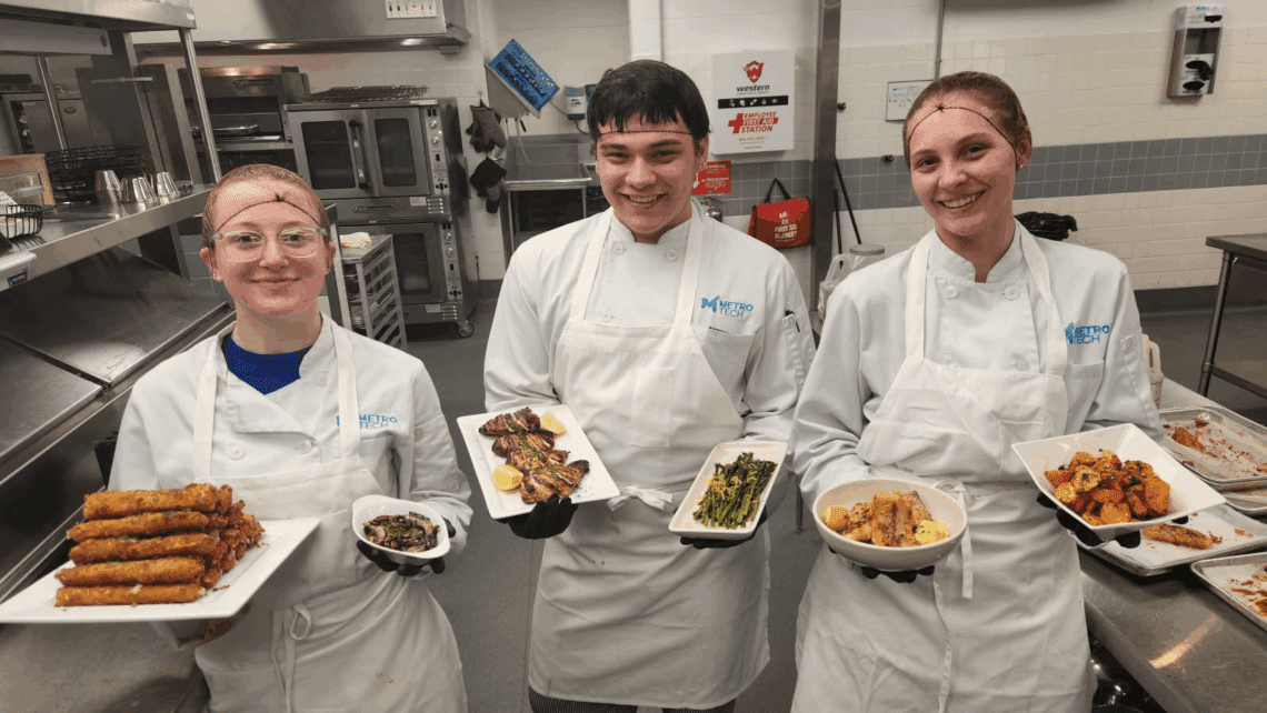 Three Sooner Job Challenge associates in chef uniforms holding plated dishes at Metro Tech.