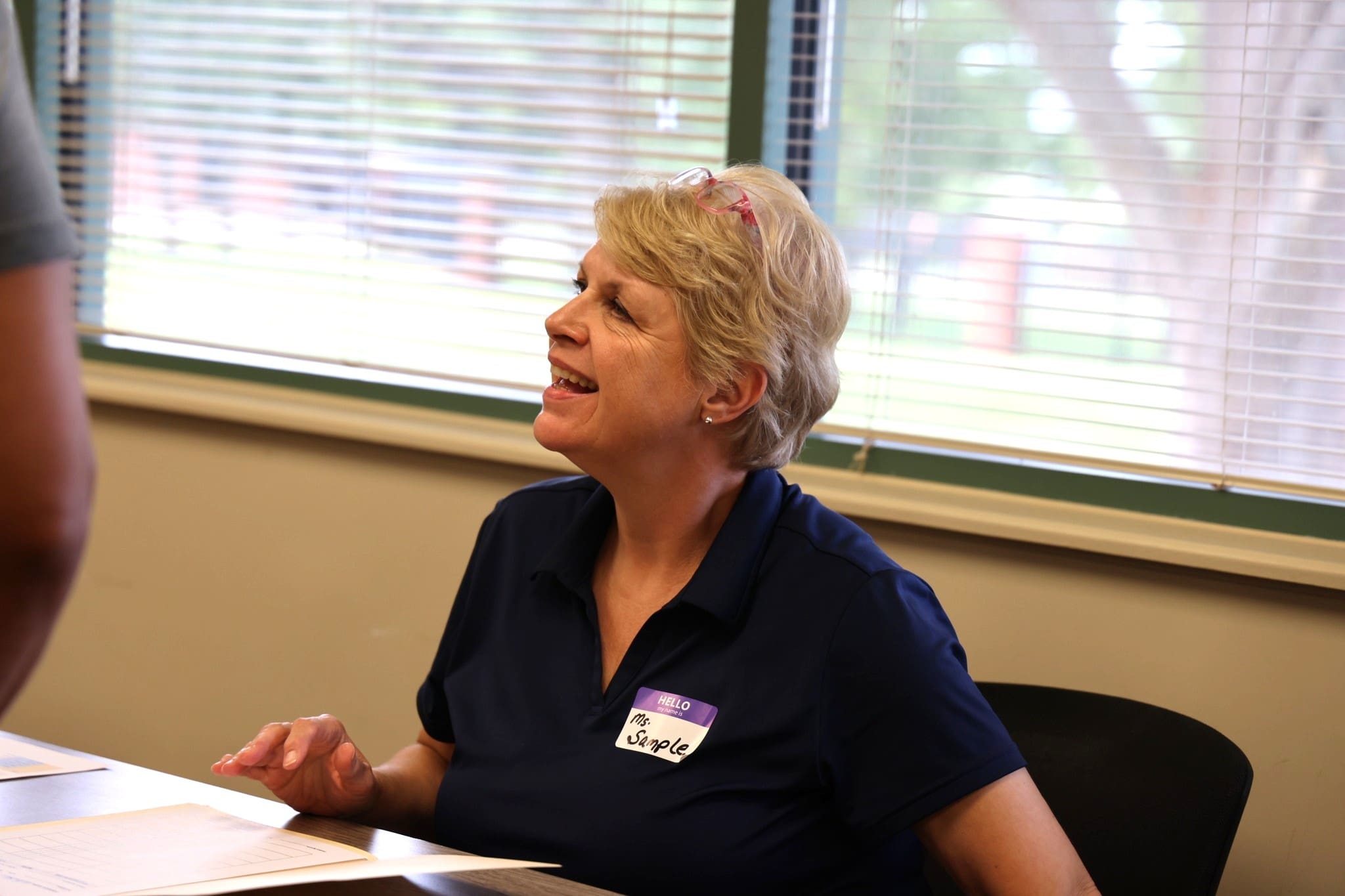 brightened nurse picture An SJC staff member is sitting at a table looking up at families as they turn in paperwork. She is smiling.