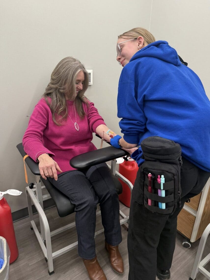Associate draws blood from Ms. Master's left arm. Both are smiling.