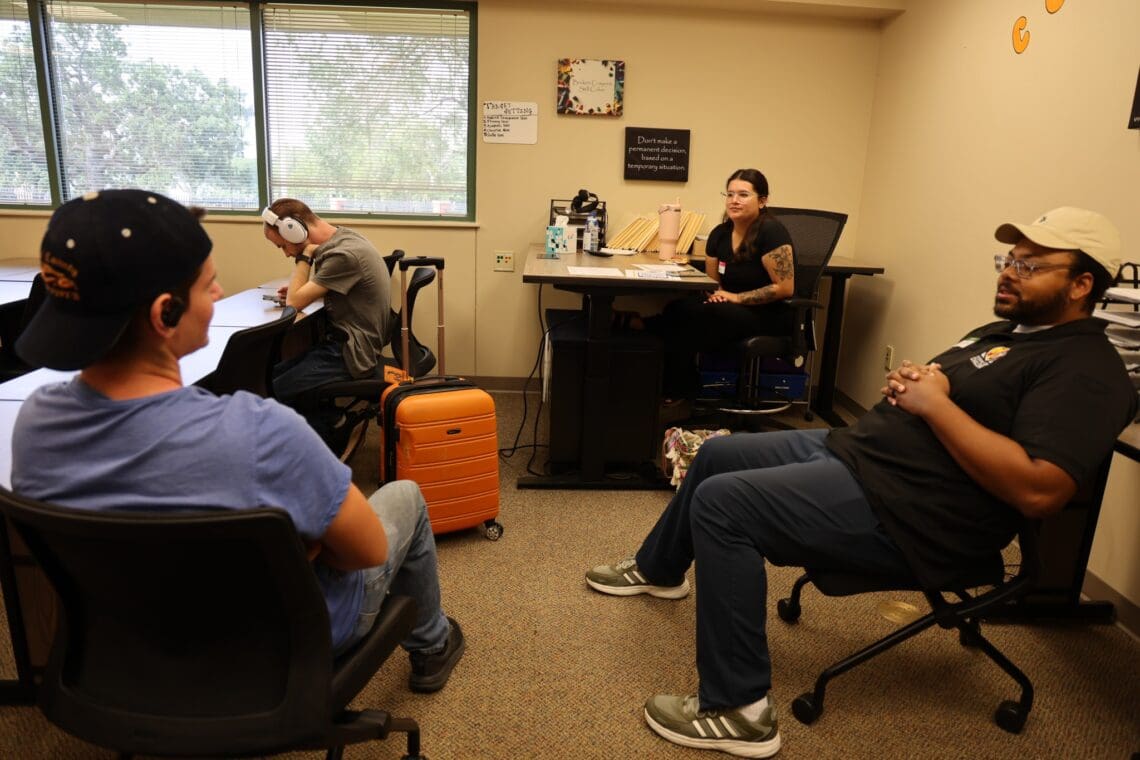 TWo staff members sit with Associates in waiting area. One Associate is talking to one staff member while the other staff member listens. 