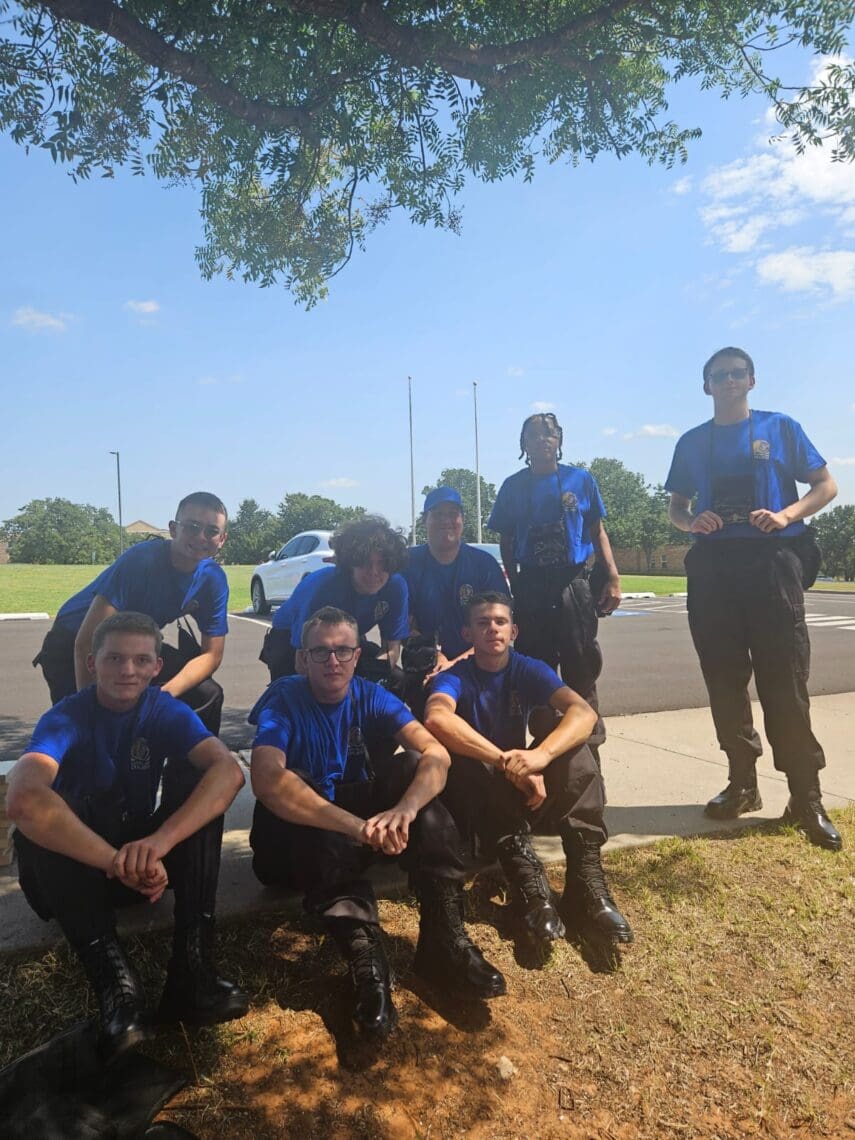 Group picture of 8 Associates sitting and standing together outside under a tree.