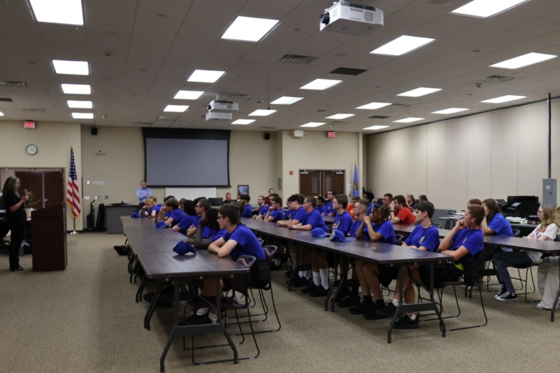 Program Director stands in front of group of seated associates with microphone, welcoming them to the program. - taken from the front facing Associates