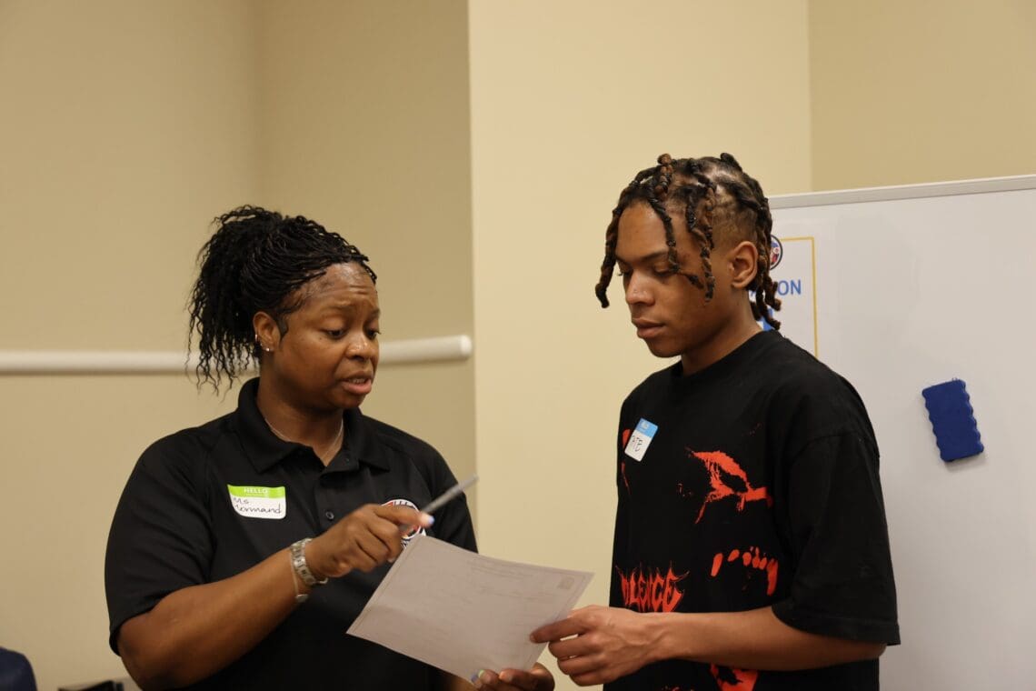 Associate checks in with staff member. Both are holding and looking at a piece of paper while staff member explains something.