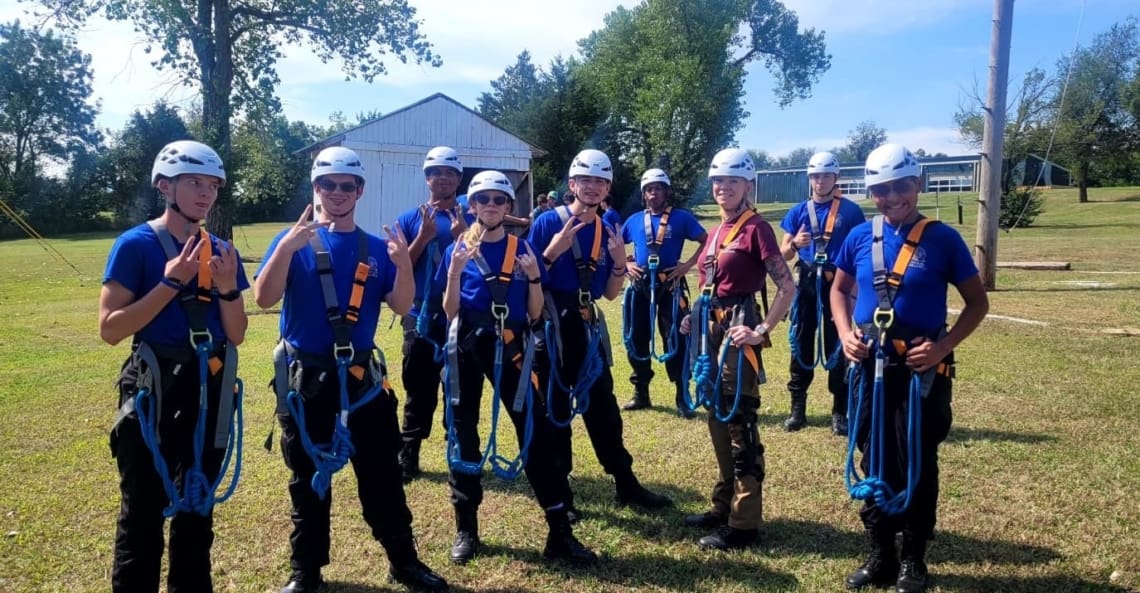 Group picture of several Associates in ropes course gear (harness and helmet).