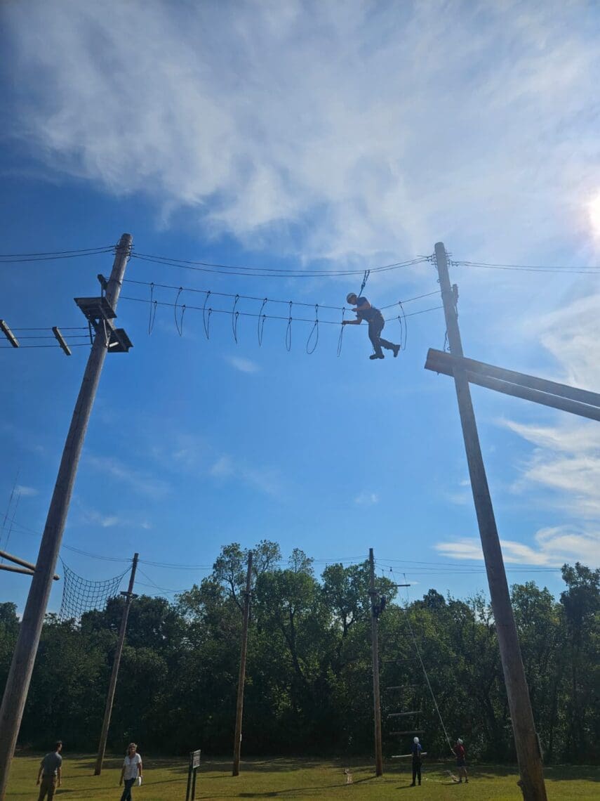 Associate is seen high above the ground, moving across a ropes course.
