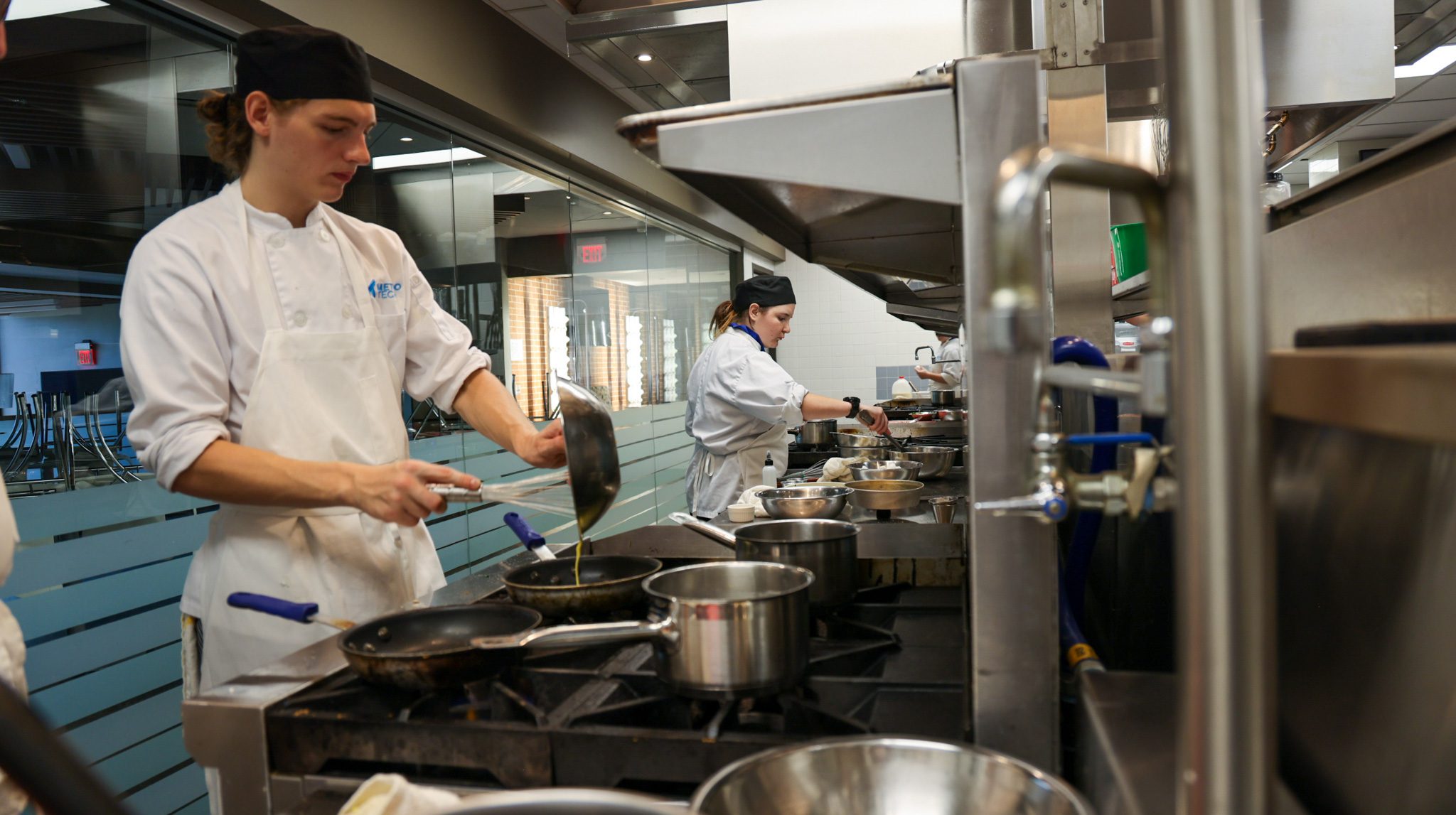 Male student and female student cooking on gas stoves.