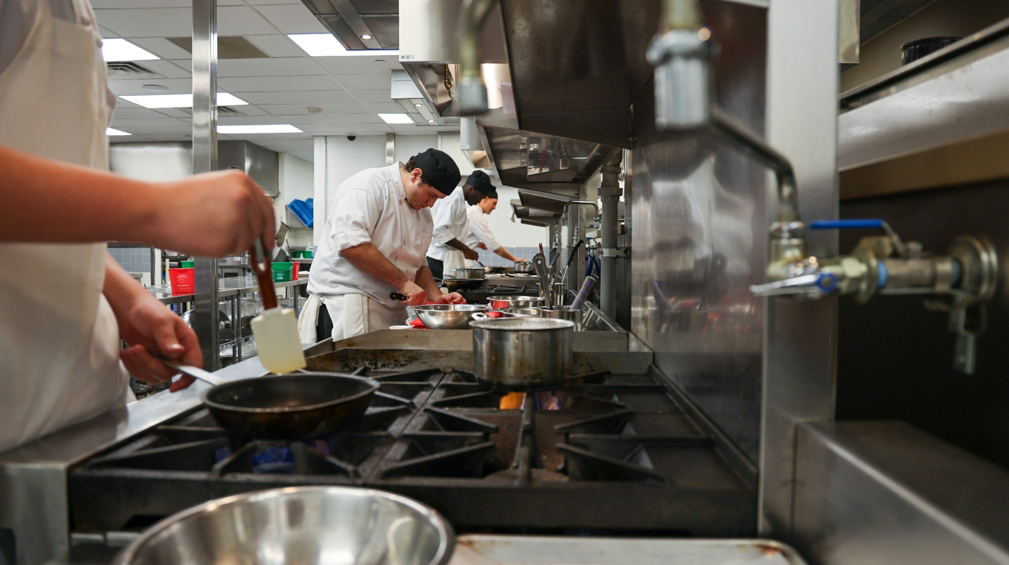 Line of stoves with a group of males students cooking on them.