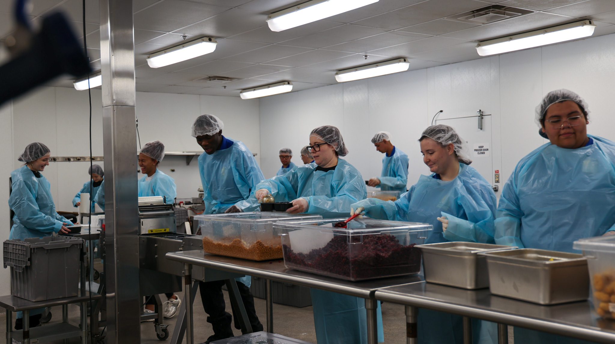 Assembly line of students packing meals into individual trays.