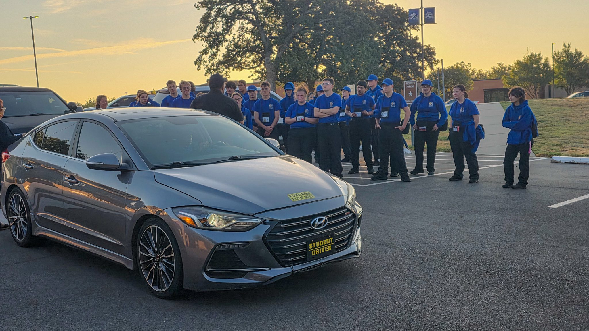 Group of students standing behind a car waiting turn at drivers ed.