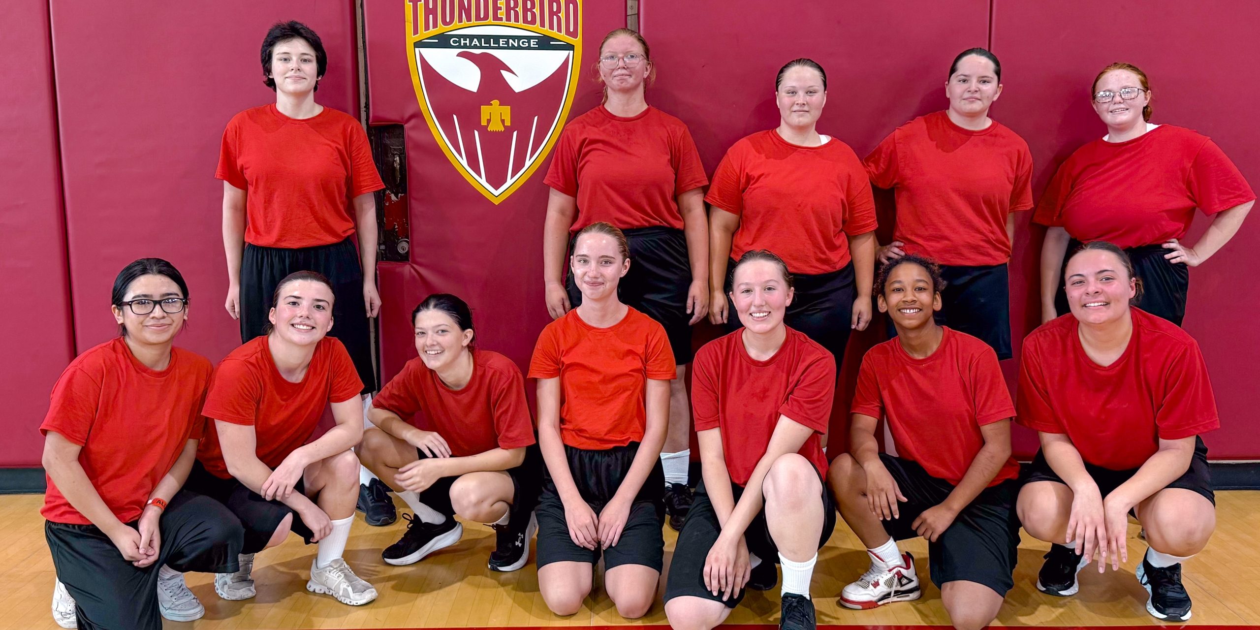 Platoon of female students under the Thunderbird logo in a gym.