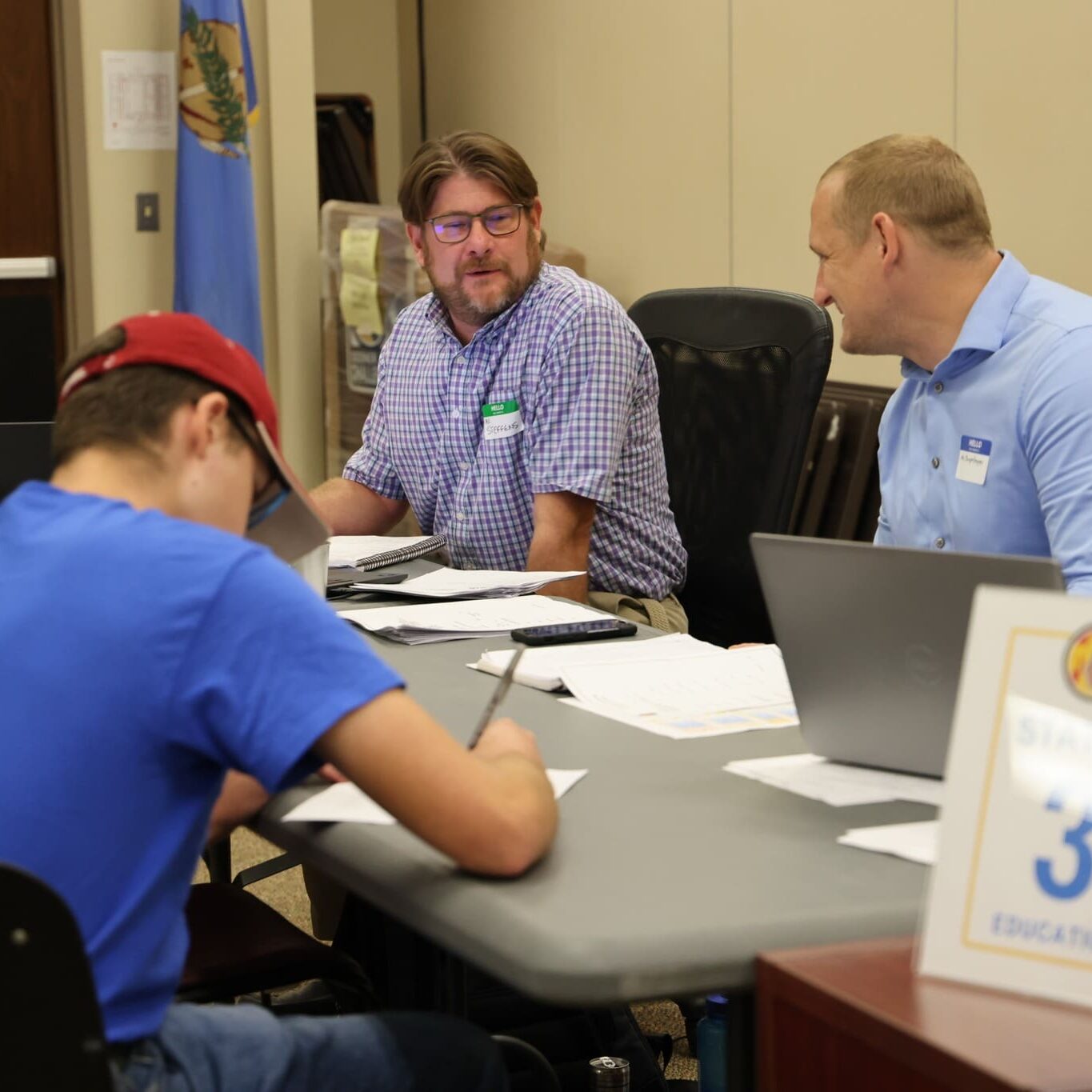 534306452_122185509038588319_3694427101935495755_n Two staff members talk to each other and smile as an Associate sits across the table filling out paperwork.