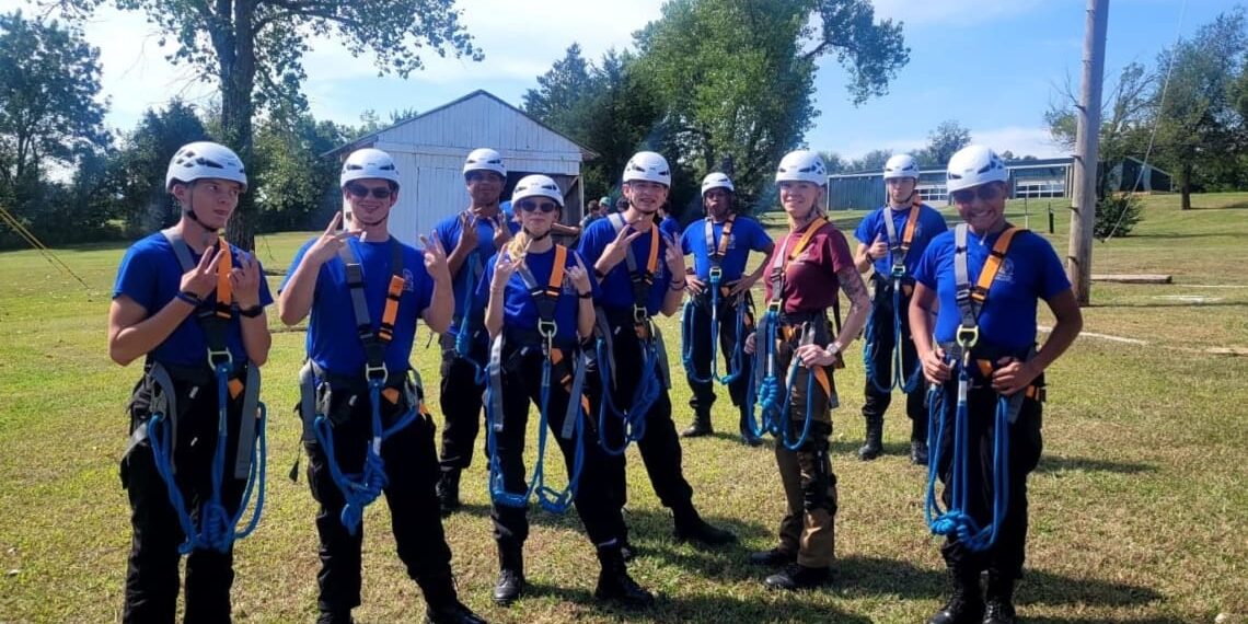 Group picture of several Associates in ropes course gear (harness and helmet).