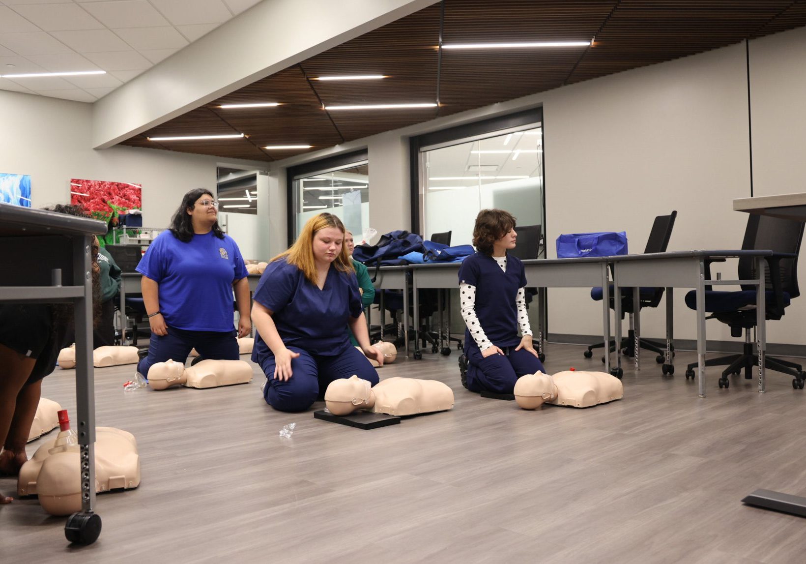 Three CNA students on the floor with CPR dummies in front of them.