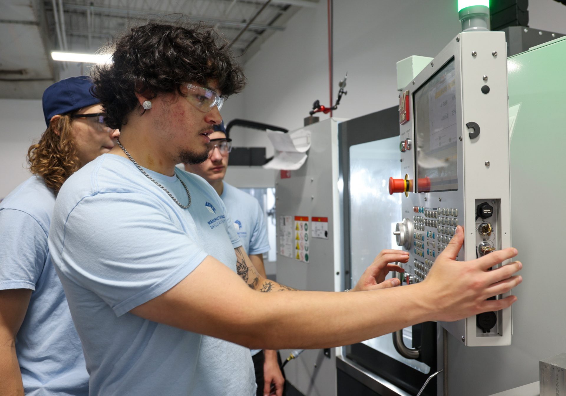 Three male students looking at a CNC Lathe programming panel.