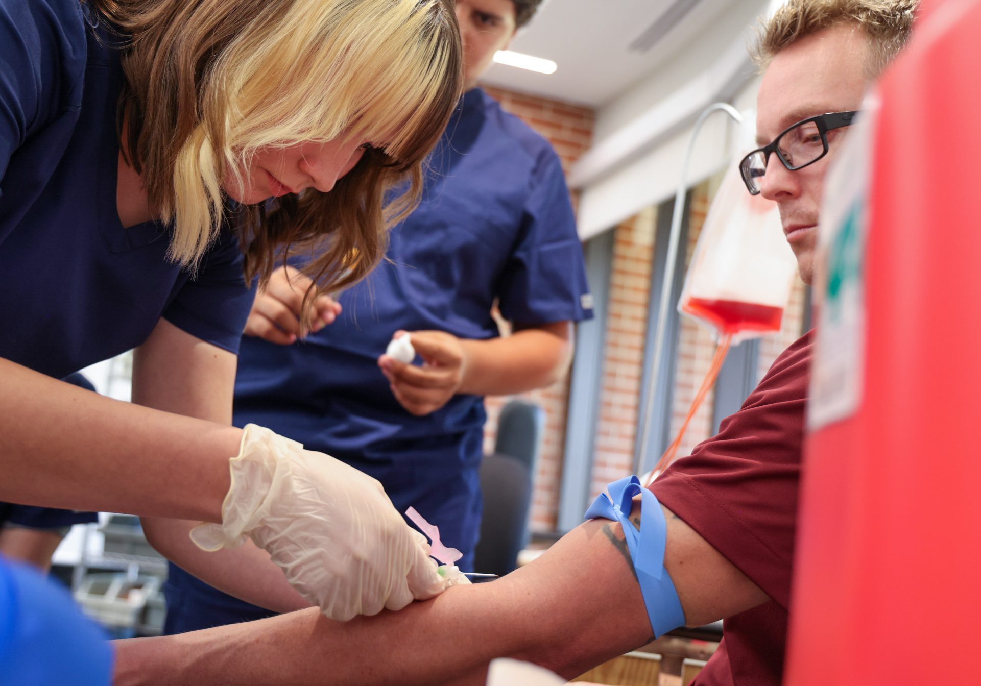 Female phlebotomy student sticking a needle in a male patient.