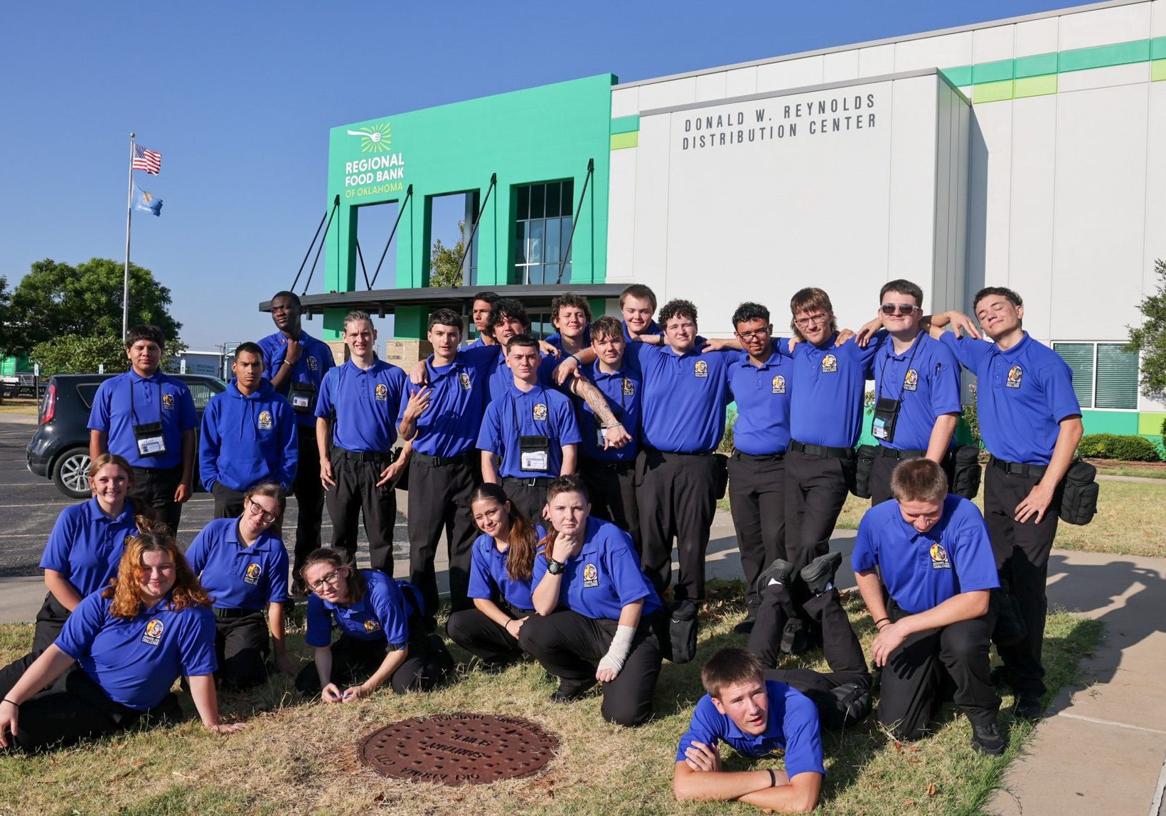 Group of students with one row standing and the other row sitting on the ground in front of the OK Regional Food Bank.
