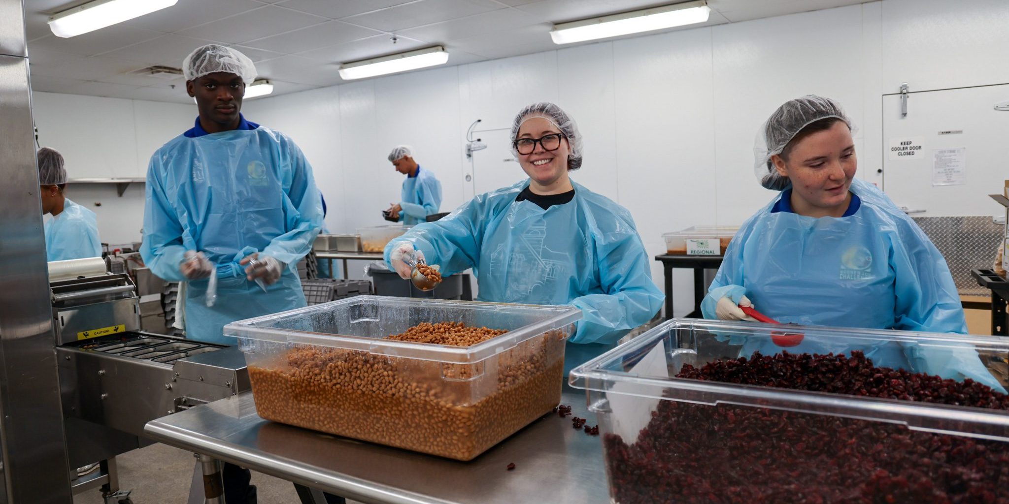 A black male and two female students putting food into single serving containers.