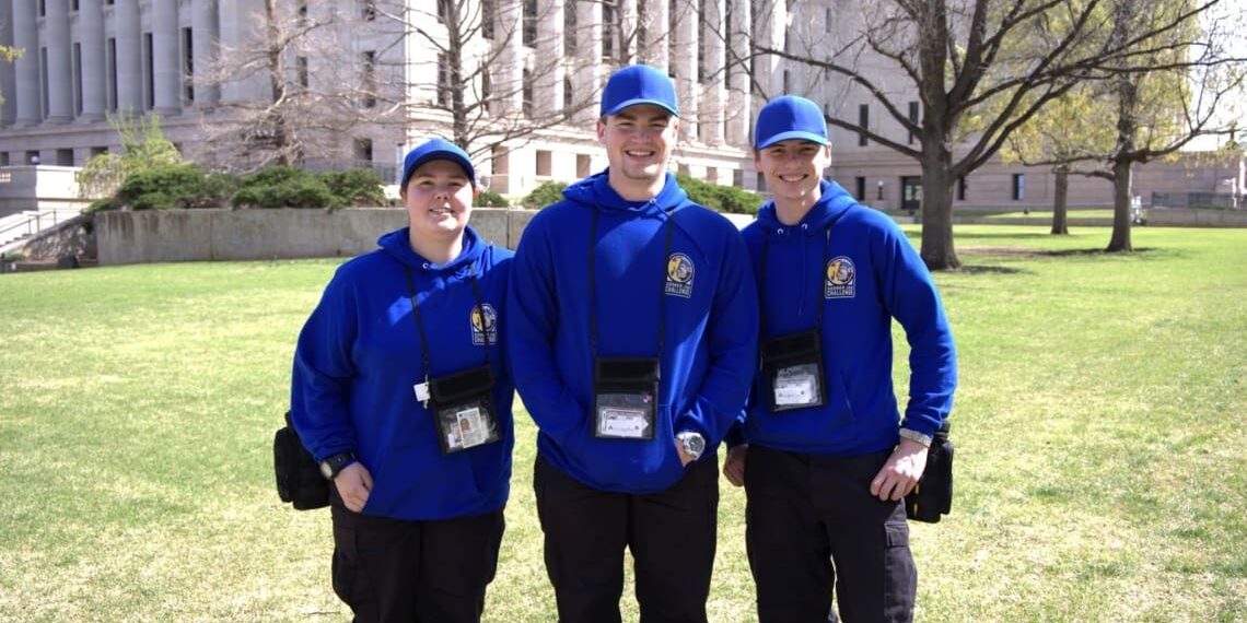 SJC_capitol-close-up Three Sooner Job Challenge participants in blue uniforms standing in front of the Oklahoma State Capitol